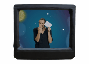 Ein Fernseher, wo man eine Personen sieht: Eyk. Er hält einen Brief hoch und lacht.